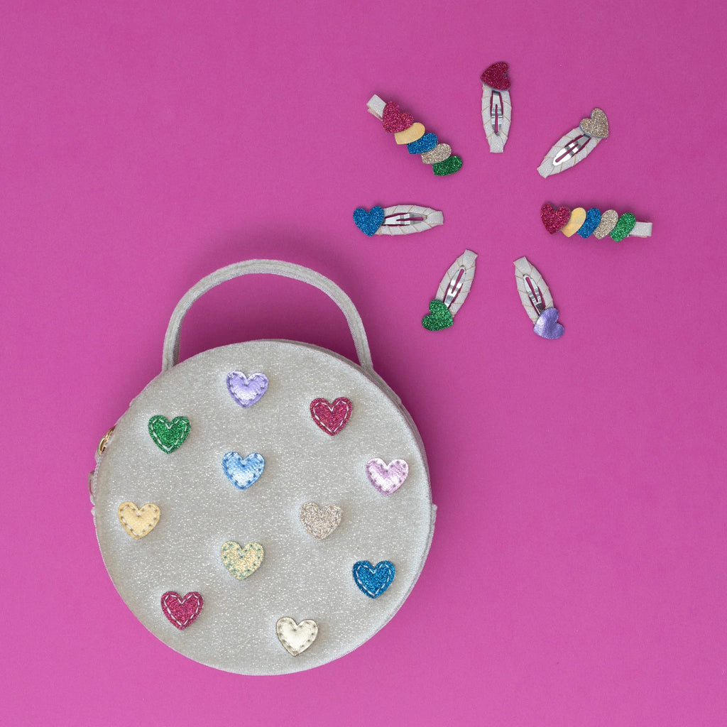 Colorful glitter heart hair clips and matching sparkly handbag on pink background – fun and playful kids accessories by Mimi & Lula.