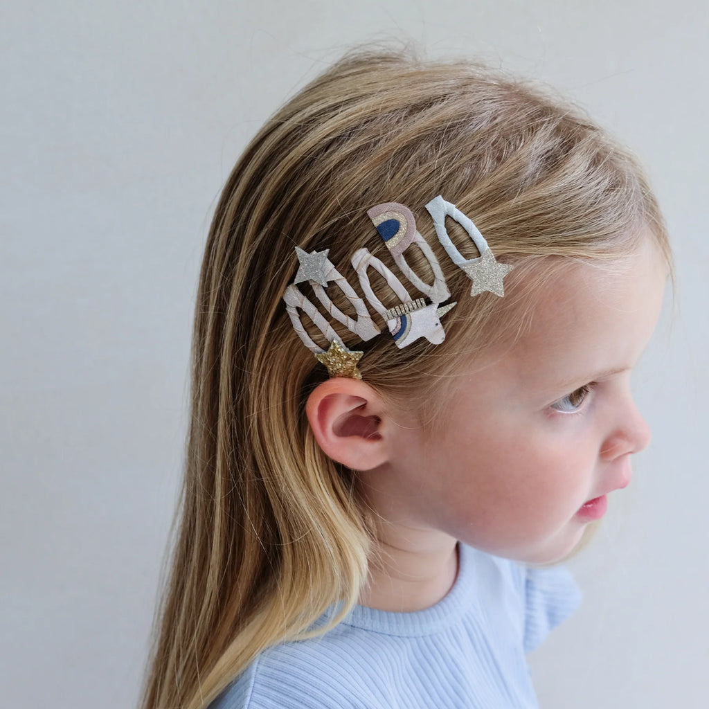 Young girl wearing multiple Mimi & Lula Celeste Mini Clic Clacs with glitter stars, unicorns, and rainbows in her hair.