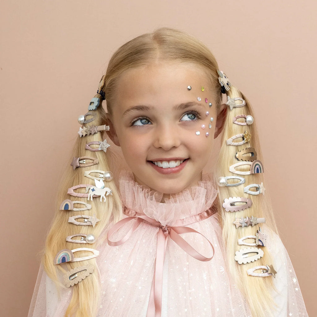 Smiling girl with pigtails decorated with multiple Mimi & Lula Celeste Mini Clic Clacs in glitter star, rainbow, and unicorn designs.