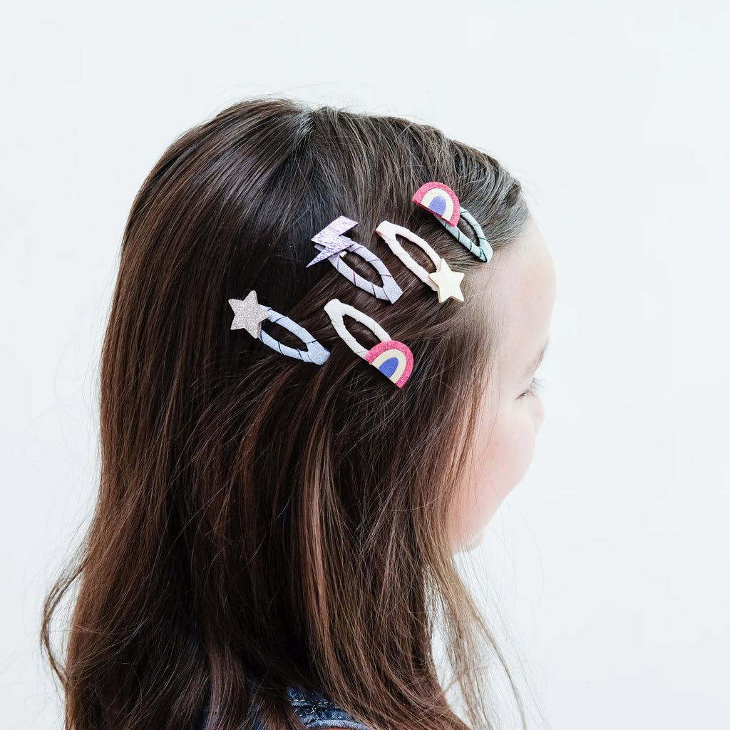 Girl with brown hair wearing several Mimi & Lula Rainbow Mini Clic Clacs featuring rainbows, stars, and lightning bolts.