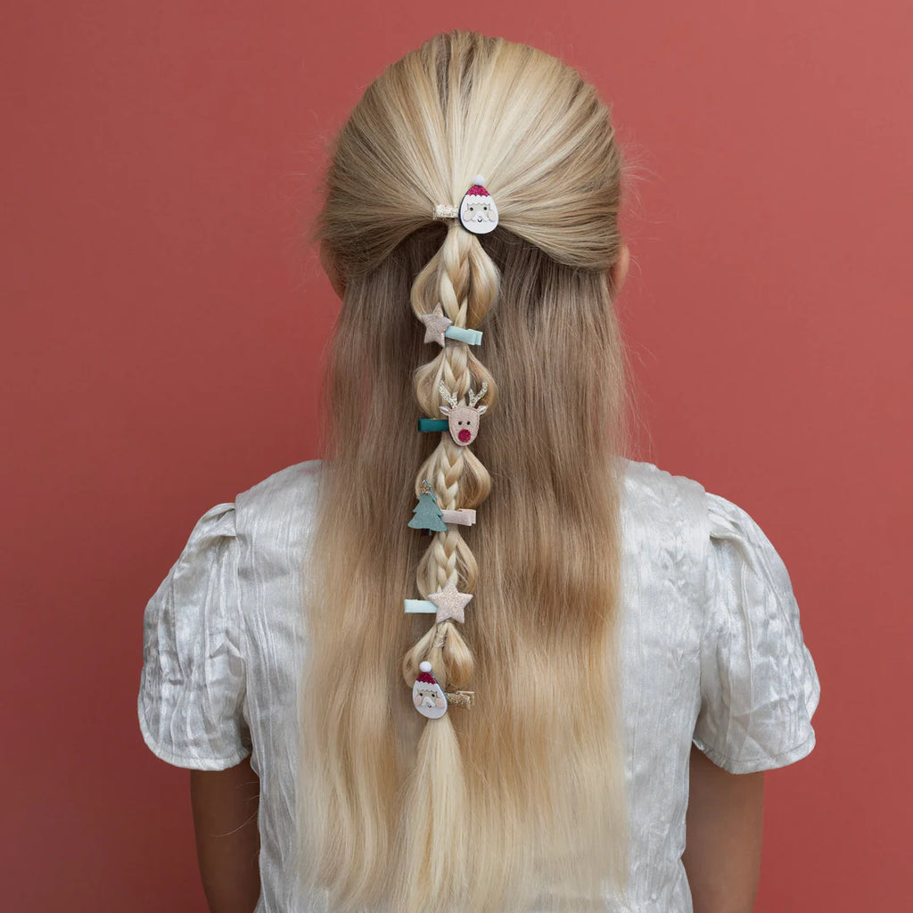 Child with long blonde hair styled with Santa, star, and reindeer Mimi & Lula clips for Christmas.
