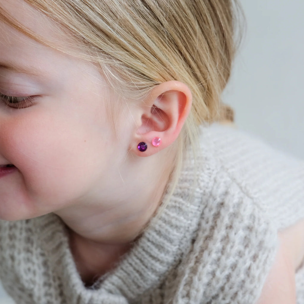 Smiling girl showing Mimi & Lula stick-on earrings on ear
