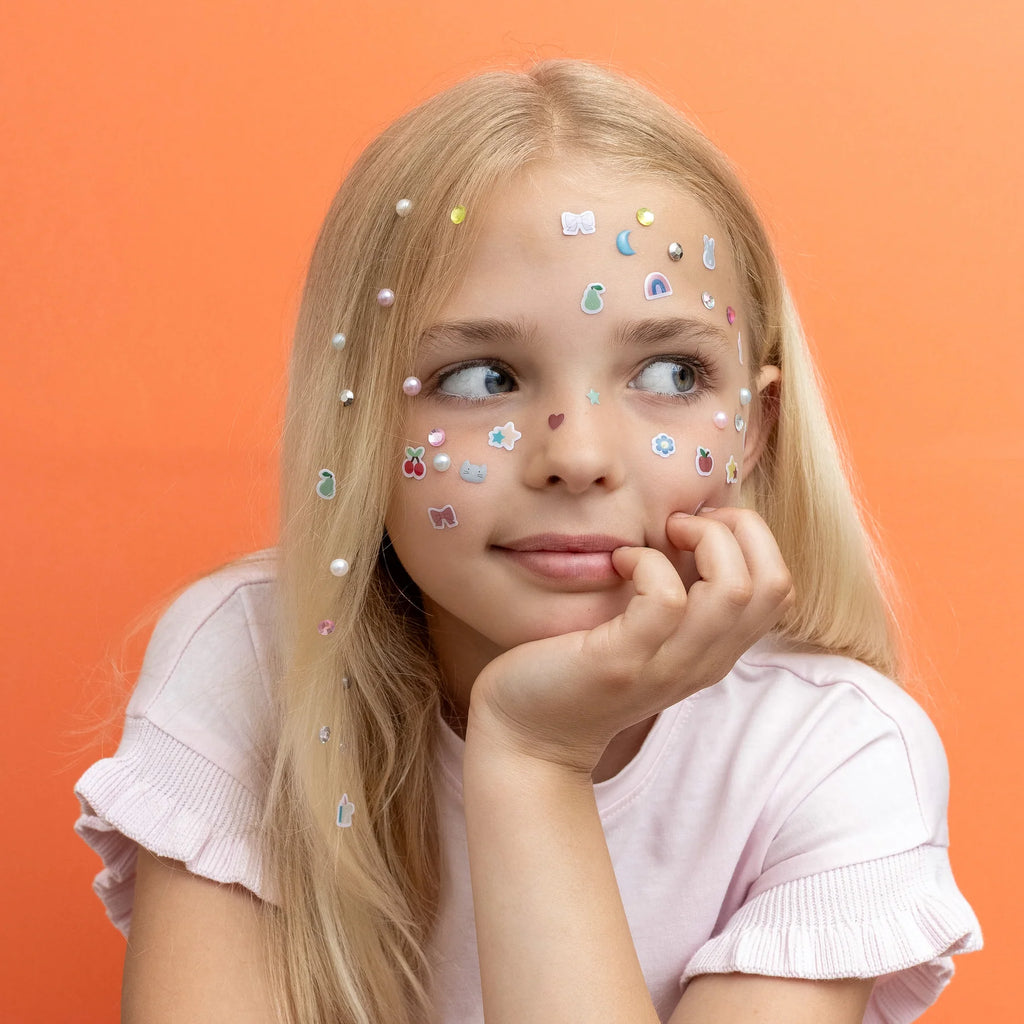 Child with creative sticker and gem face art using Mimi & Lula stick-on earrings
