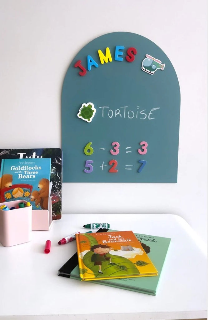 Teal Mini MagPlay decal set up as a learning station with magnetic name letters, math problems, and themed magnets, alongside children's books and colourful stationery.