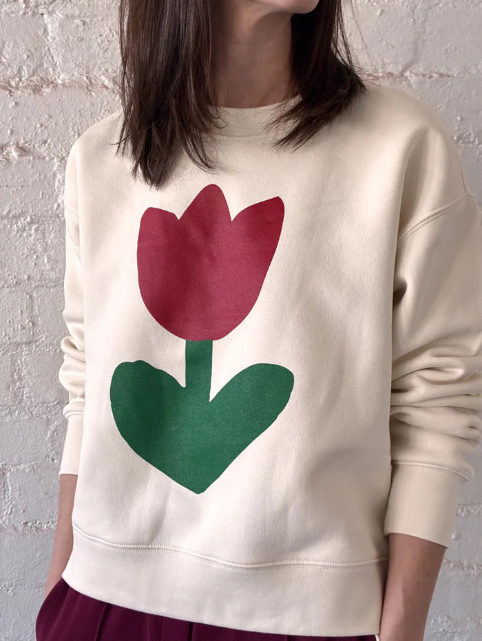 Model wearing the Mosey Me Tulip Sweater in Ecru, showing the oversized relaxed fit and eye-catching red and green tulip design across the front.