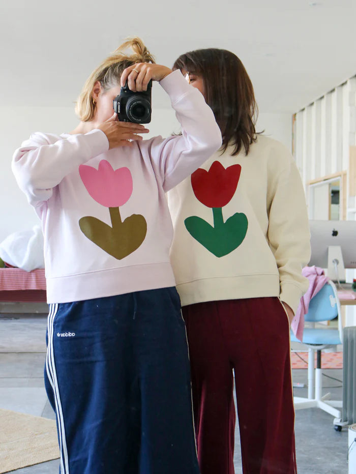 Two women standing side by side, one in Ecru and one in Orchid Tulip Sweater, showing the matching tulip motif on both sweatshirts in a casual setting.