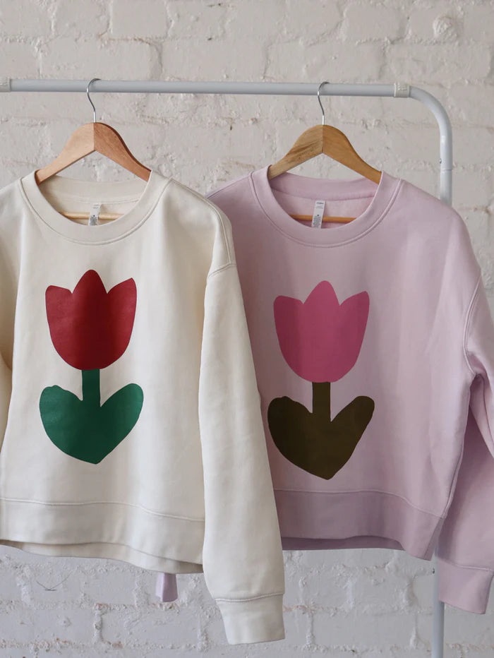 Two Mosey Me Tulip Sweaters hanging on wooden hangers—one in Orchid and one in Rust—displaying the graphic floral prints and pastel colour options.