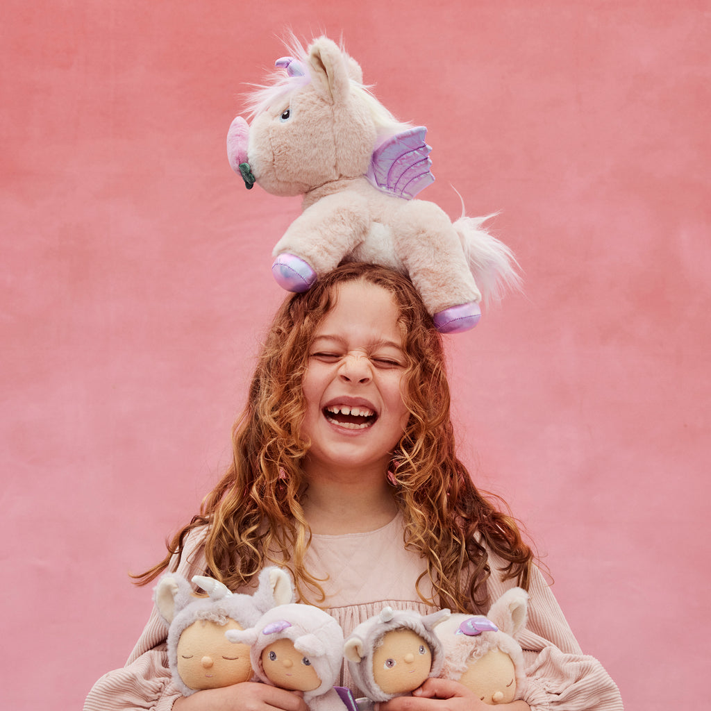 Shimmer unicorn plush balanced on a girl’s head – Playful moment with posable unicorn showing lavender horn and purple wings.