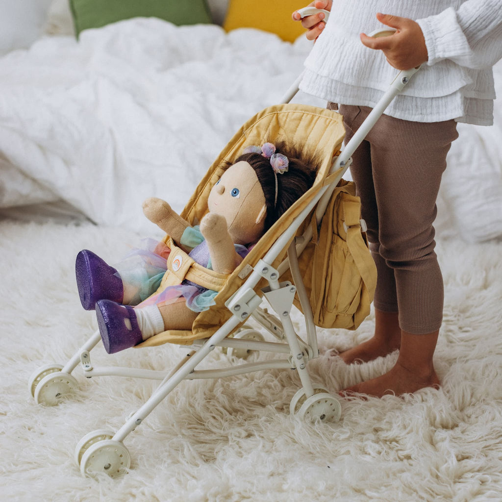 Child playing indoors with Dinkum Doll in honey stroller – Toddler arranging doll in honey quilted stroller on fluffy rug.
