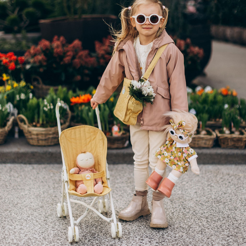 Toddler pushing honey stroller with doll outdoors near flowers – Child enjoying pretend play, strolling plush dolls in honey stroller.