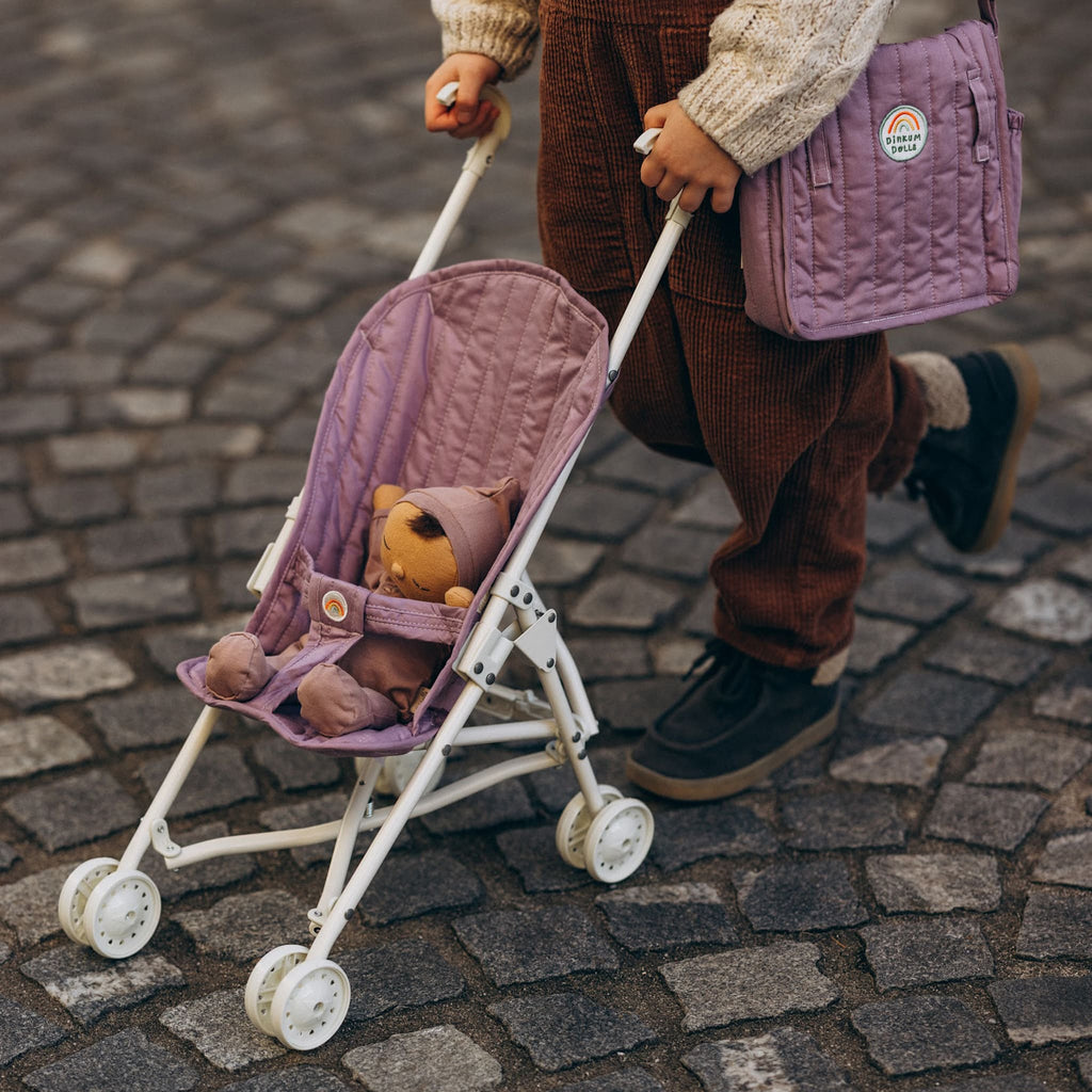 Toddler pushing stroller outdoors with doll inside – Lavender stroller being wheeled along cobblestone street during play.