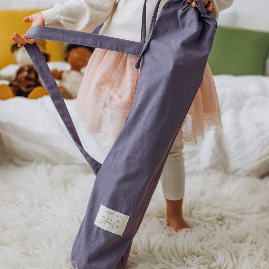 Child holding lavender stroller carry bag indoors – Toddler carrying folded stroller in lavender cotton drawstring bag.