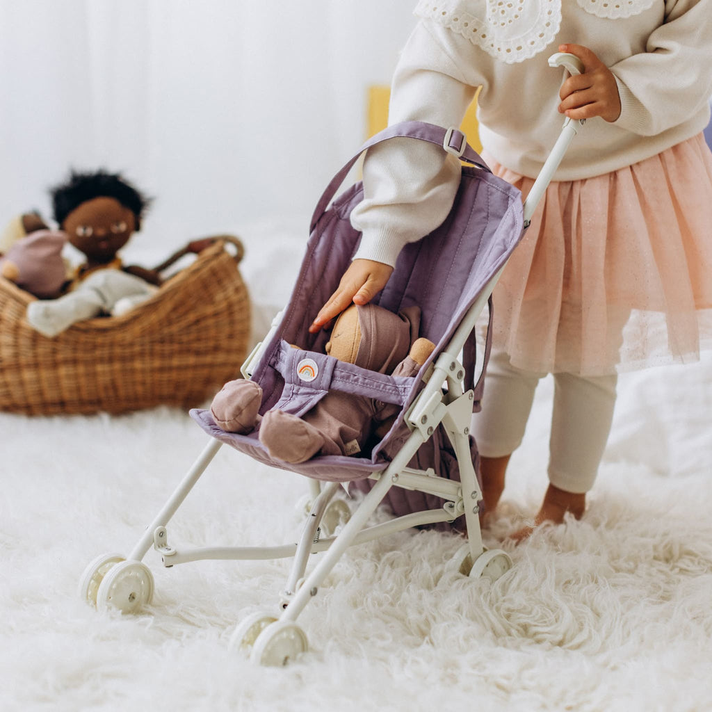 Toddler pushing Dinkum Doll in lavender stroller indoors – Child on fluffy rug walking doll in stroller for pretend play.
