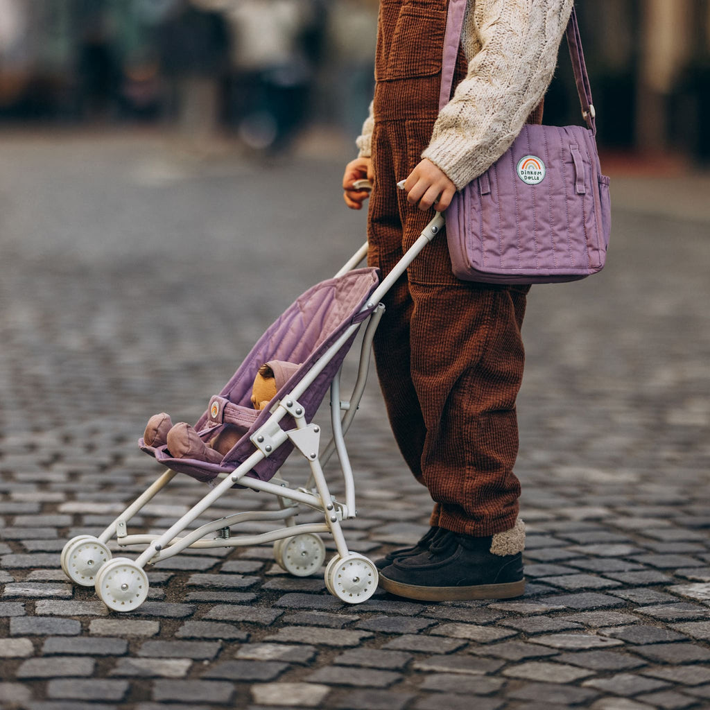 Toddler pushing stroller outdoors with doll inside – Lavender stroller being wheeled along cobblestone street during play.