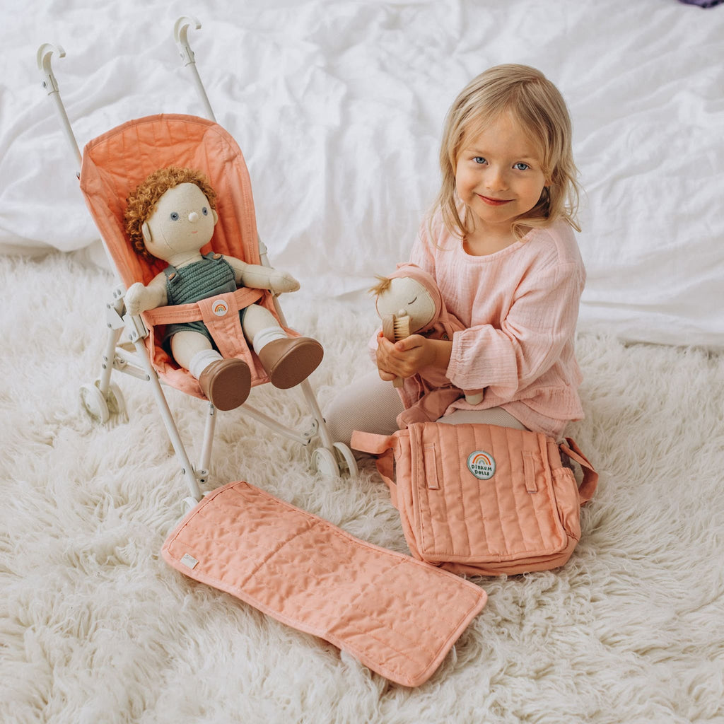 Toddler sitting beside Sollie Stroller indoors – Child on rug playing with doll in rose stroller, quilted seat visible.
