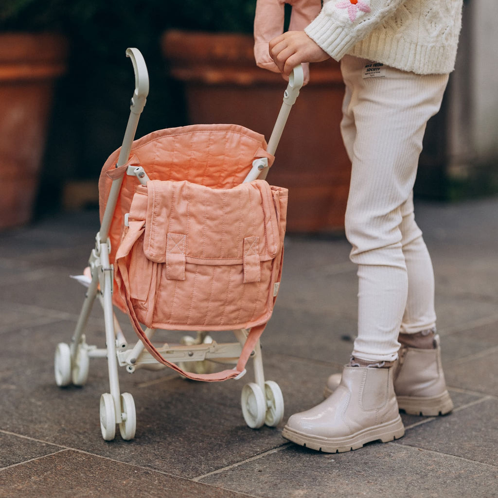 Close-up of toddler pushing stroller outdoors – Focus on child’s hands pushing the rose pink doll stroller with matching changing bag attached.