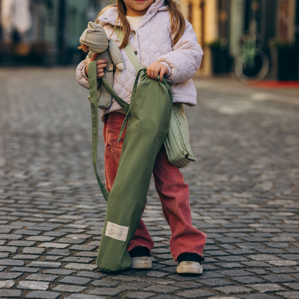 Child holding folded Sollie Stroller carry bag – Little one carrying sage cotton canvas stroller bag with shoulder strap.