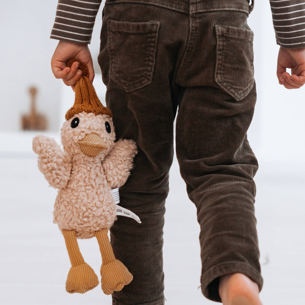 Petunia Duck plush toy hanging from a child’s hand, showing detailed plush texture, corduroy accents, and warm knitted beanie.
