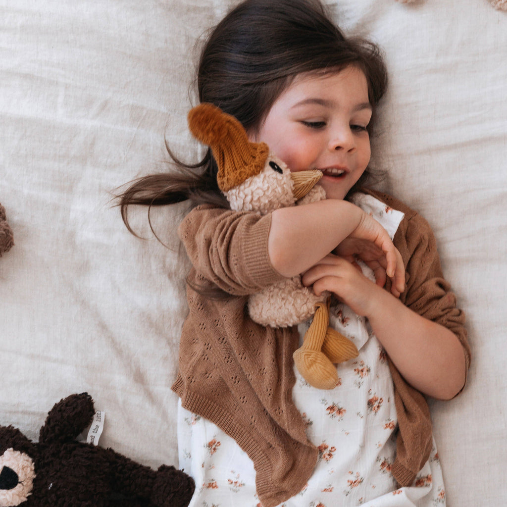 Child cuddling Petunia Duck plush toy in bed, highlighting cosy texture and comforting design.