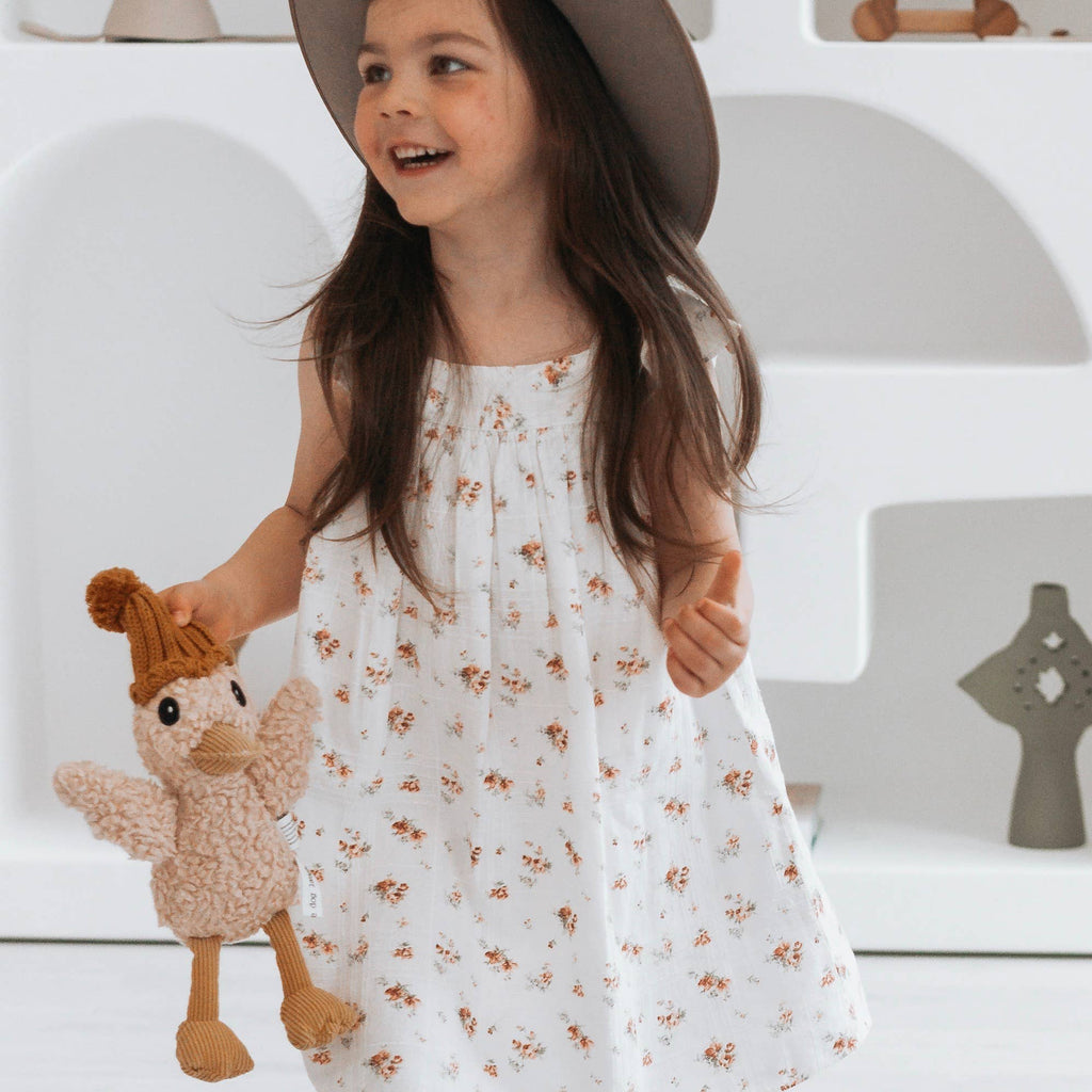 Smiling child in white floral dress holding Petunia Duck plush toy, showing friendly design and whimsical style.