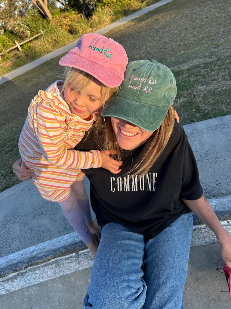 Child wearing the pink "Handful" cap paired with a green version, showcasing the cap’s playful design and perfect fit for kids on the go.