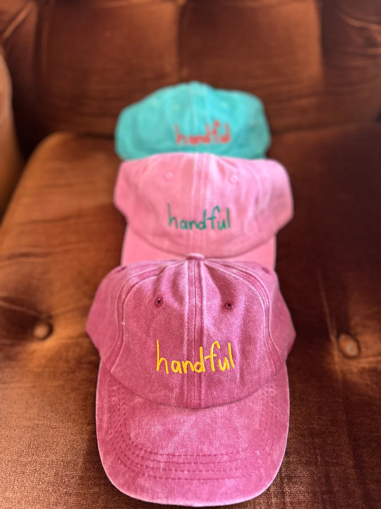 Stack of vibrant kids "Handful" caps in pink, purple, and aqua, highlighting the fun colours and front embroidery design.