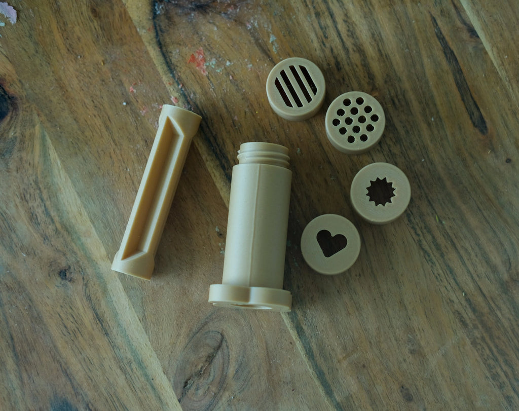 Kinfolk Pantry dough extruder set with pusher and shape lids, styled for playtime with earth-toned tools and natural materials.