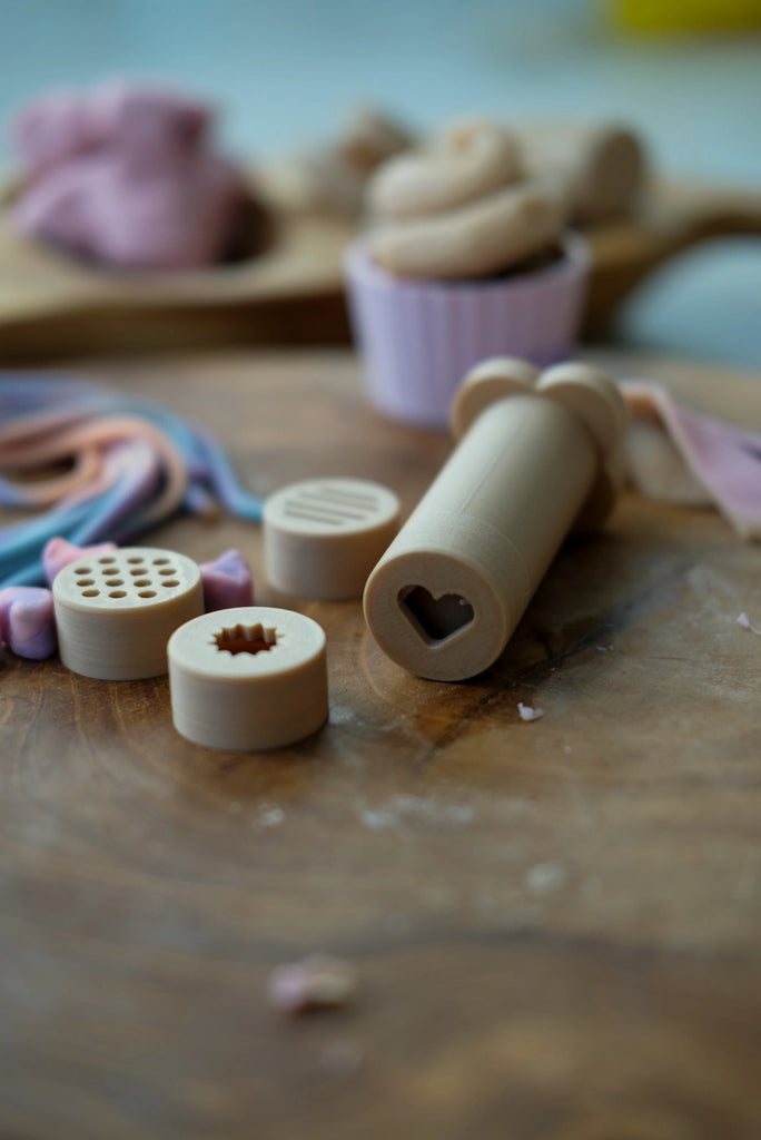 Kinfolk Pantry dough extruder set with pusher and shape lids, styled for playtime with earth-toned tools and natural materials.