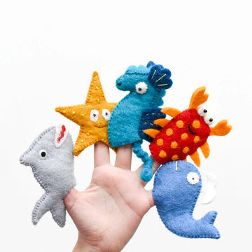 Hand holding five wool felt ocean animal finger puppets, including shark, seahorse, lobster, starfish, and whale from Tara Treasures.