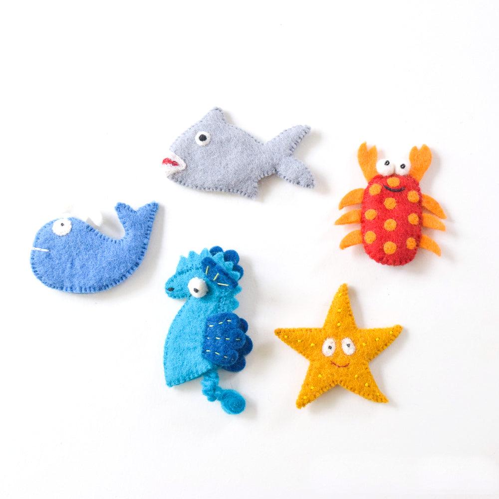 Top-down view of colourful wool finger puppets shaped like ocean animals—shark, whale, seahorse, lobster, and starfish on a white background.