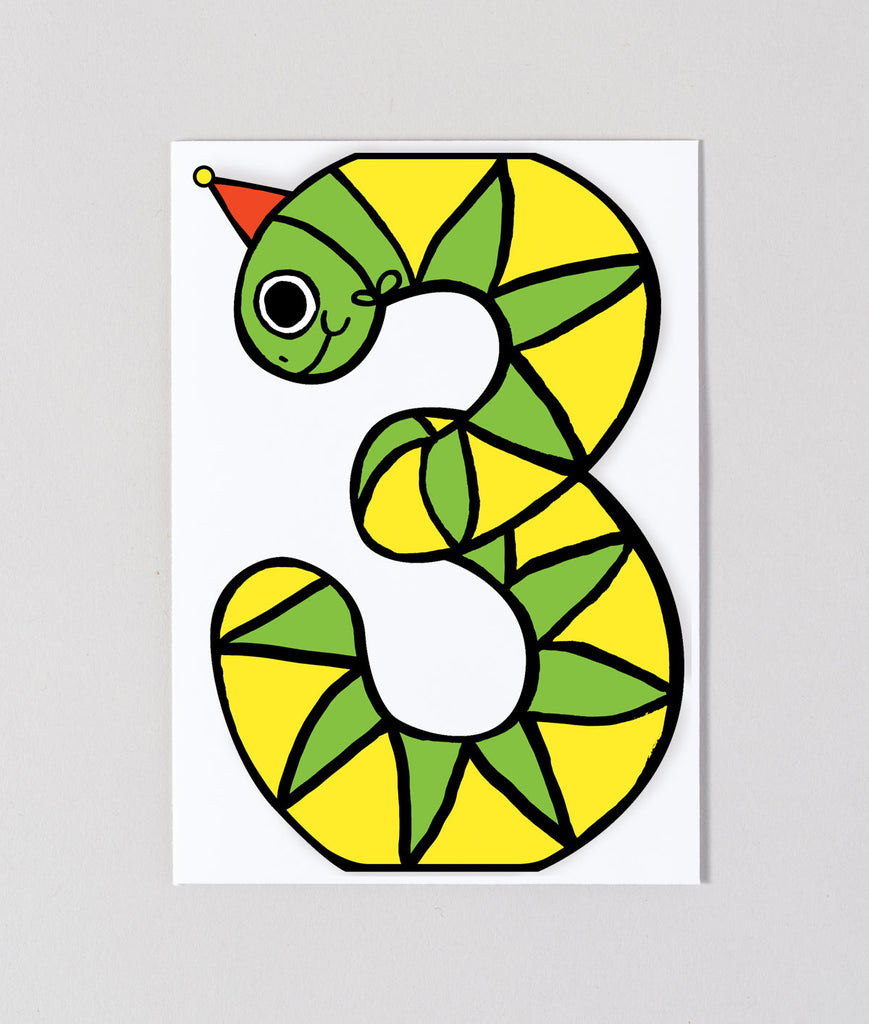Flat lay view of snake-themed third birthday card shaped like a number 3, showcasing bold lines and fun party styling.