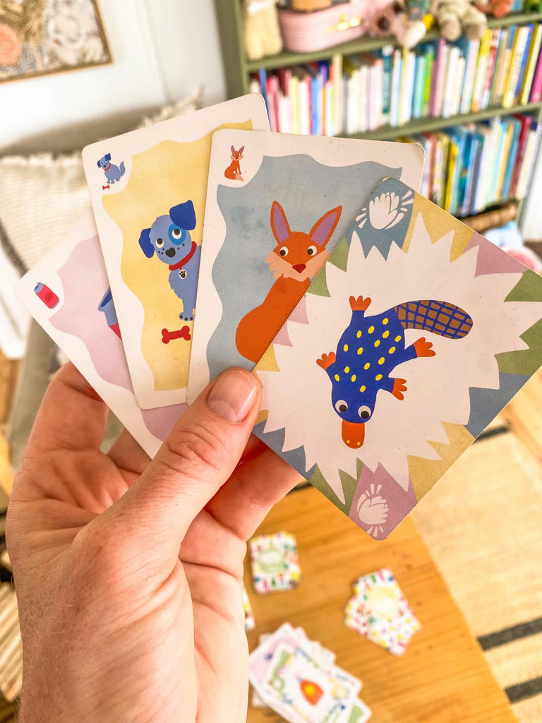 Hand holding a fanned-out selection of Sound Slam cards, revealing a variety of hand-drawn images designed to support phonological awareness through play.