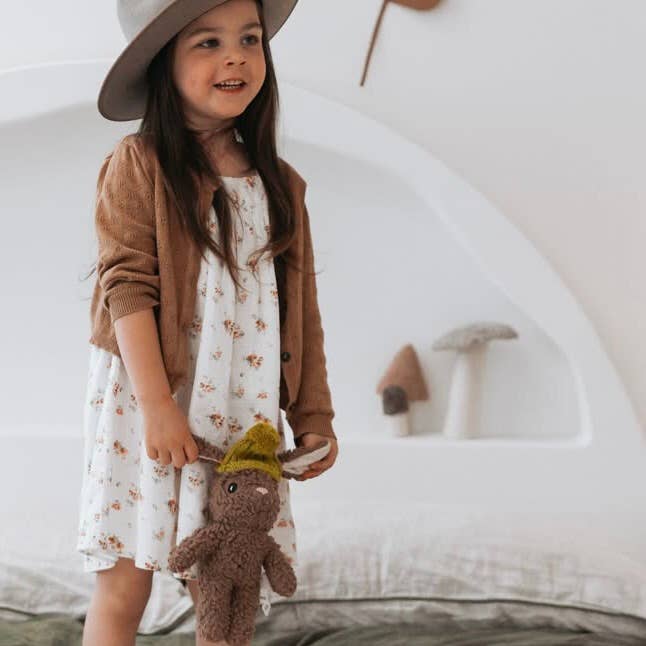 Young girl standing in a bedroom holding Stella Rabbit plush toy by her side, showcasing its soft texture and knitted beanie.