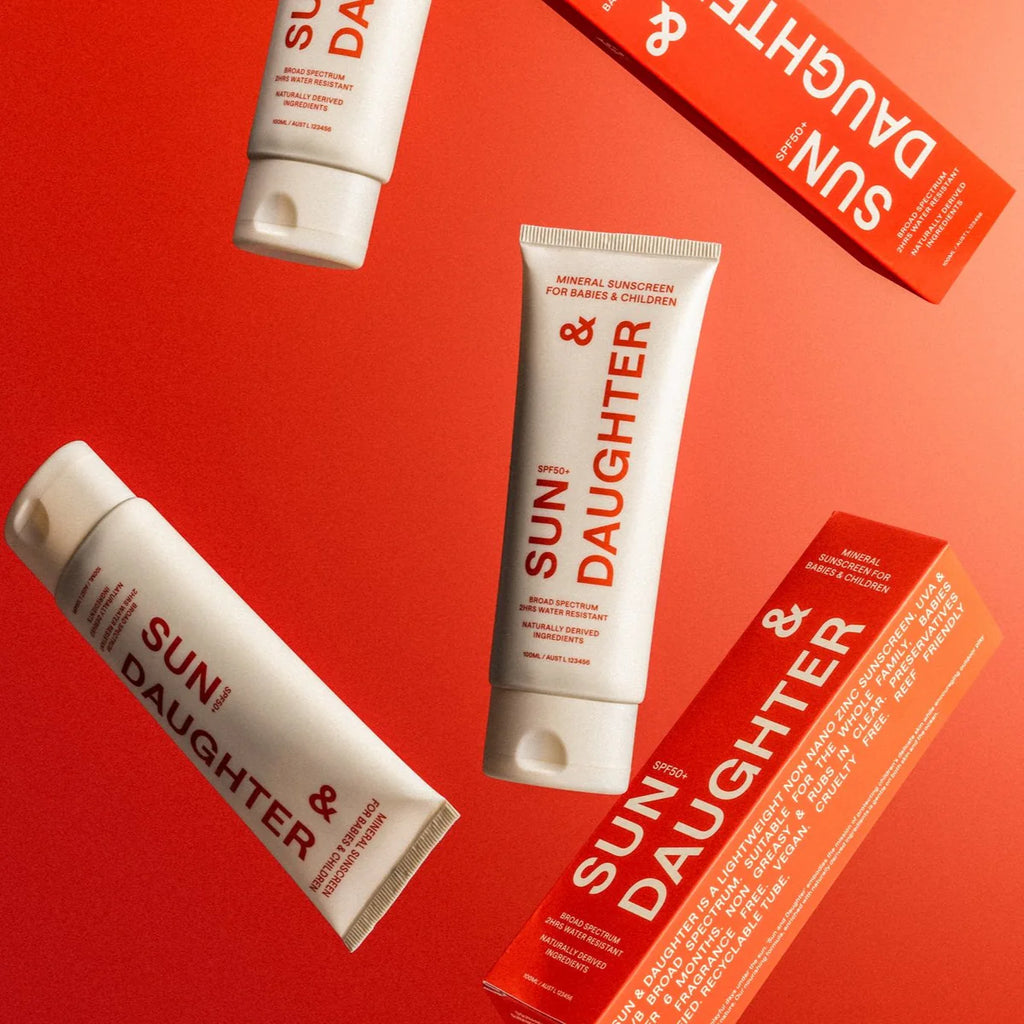 Flat lay of Sun & Daughter SPF50+ Mineral Sunscreen range including tubes and box, set against a bold red background.