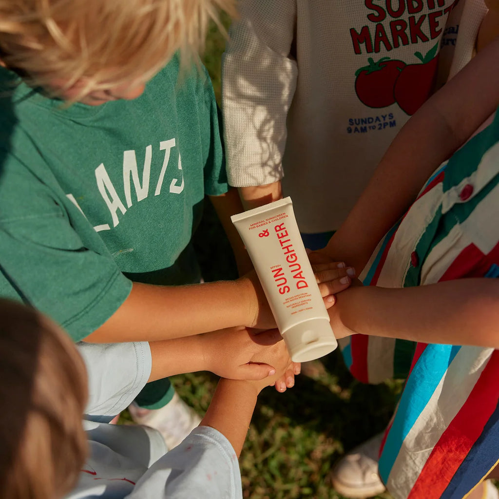 Children outdoors applying Sun & Daughter SPF50+ Mineral Sunscreen, sharing the product between hands.
