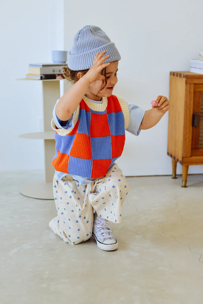 Child in the Blue Figo Beanie mid-play, styled in a bold checkered vest and cream pants with blue star prints, in a bright, modern indoor space.
