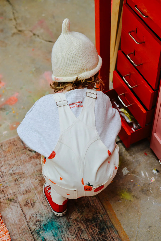 Back view of a child in a cream Teepee Beanie and fun printed outfit, crouched near a red drawer in a colourful and textured play area.