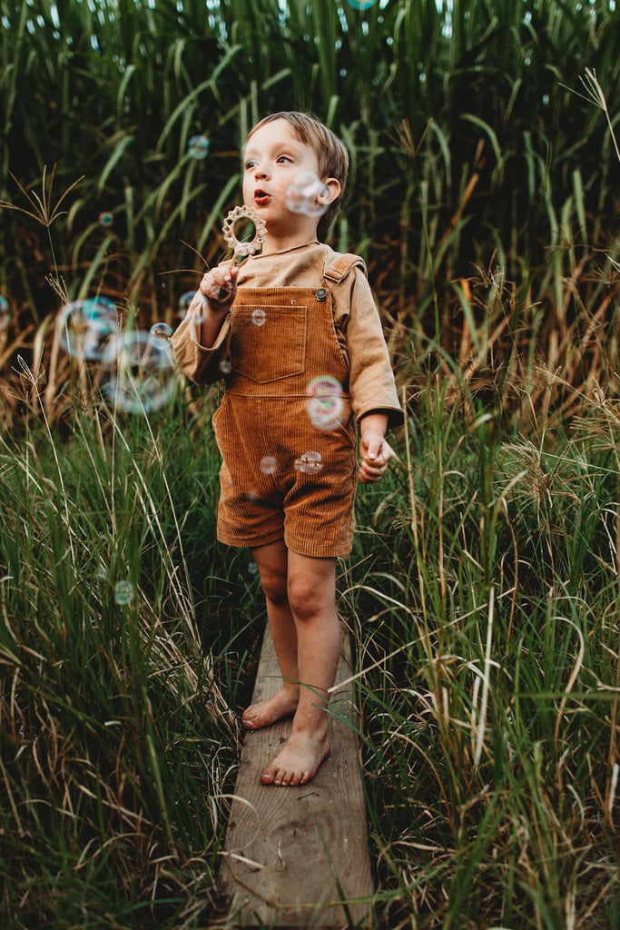Child blowing bubbles in a grassy field with a Sunflower Bubble Blower from Kinfolk Pantry.