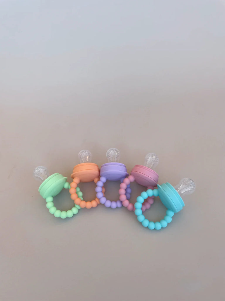 Flat lay of silicone baby feeders in aqua, lilac, pink, green, and orange – BPA-free teethers and feeders for babies 6 months and up.