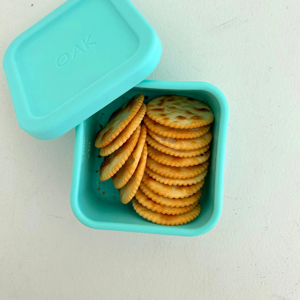 Top-down view of The Zero Waste People aqua snack container with lid ajar, showcasing stacked crackers inside a compact, eco-friendly lunch solution.