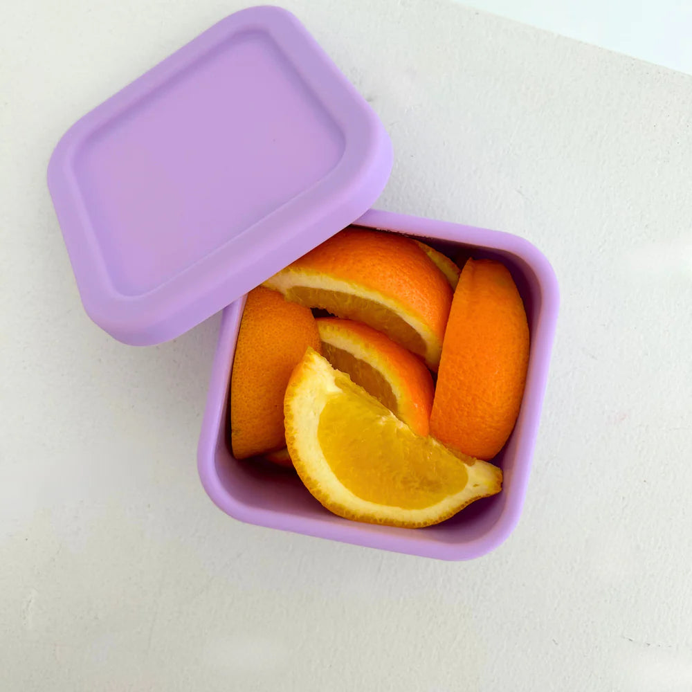 Lilac Zero Waste People snack container with lid off, showcasing orange slices inside on a white surface.