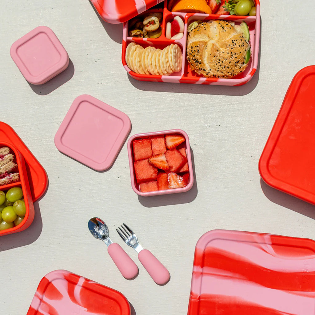 Flat lay of The Zero Waste People watermelon pink snack container with matching lunchbox and mini cutlery set, ideal for kids' lunches on the go.