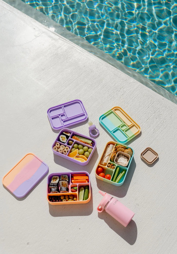 Flatlay of pastel Bento Lunchboxes and accessories by the pool – ideal reusable lunch containers for busy families on the go.