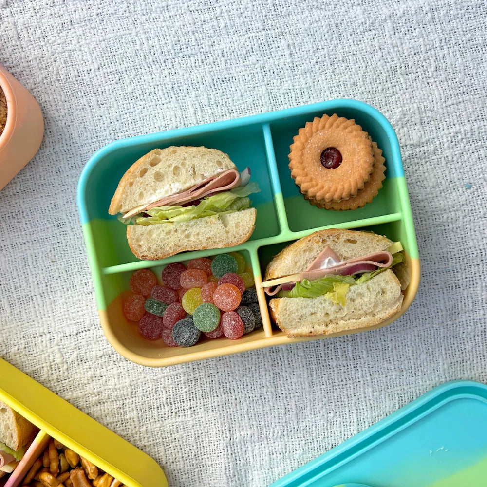 Close-up of Zero Waste People Midi Box packed with mini sandwiches, lollies, and cookie—reusable lunchbox in pastel rainbow Splice design.