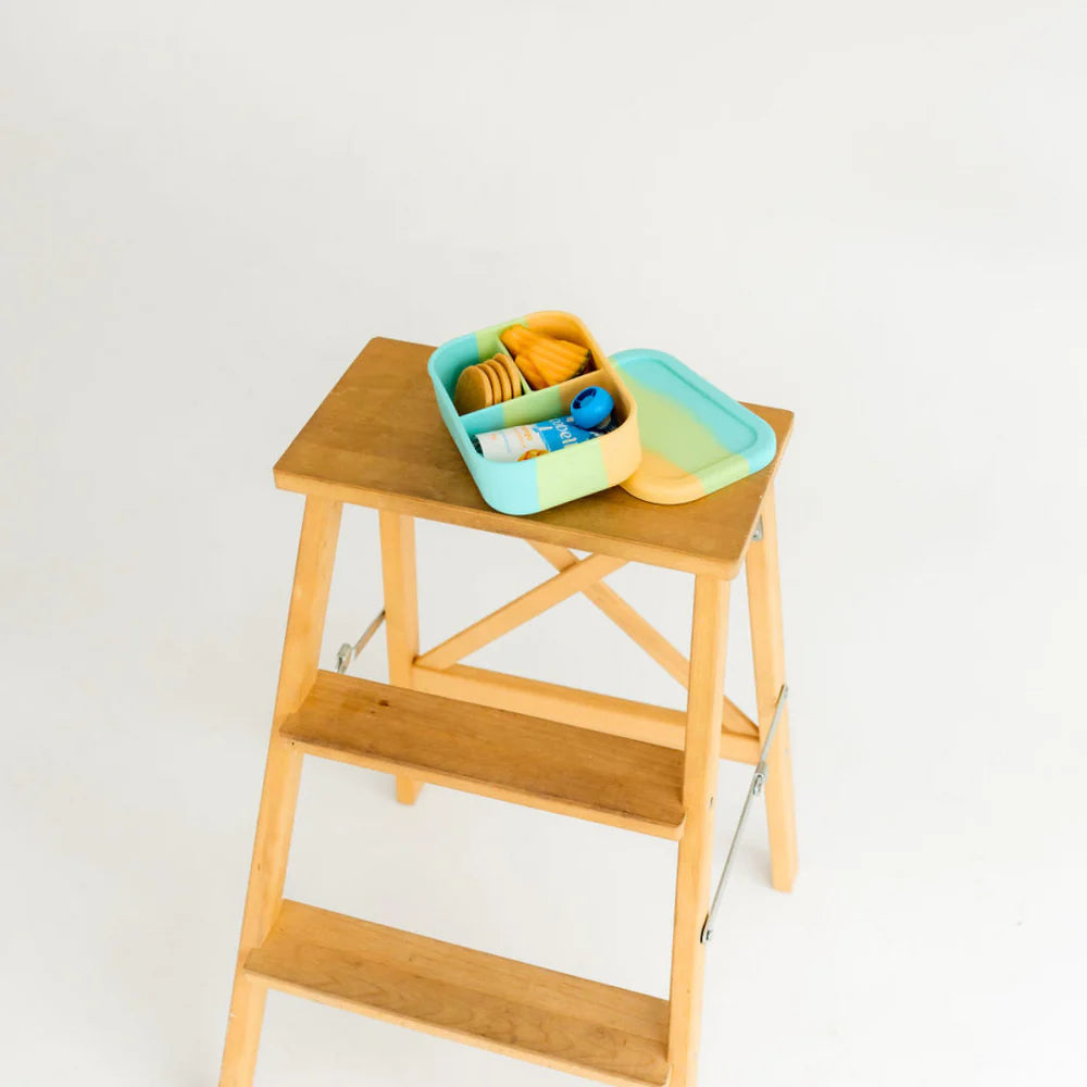 The Munchbox Mini displayed on a stool with lunch packed inside—ideal leak-proof and microwave-safe lunchbox for toddlers and kids.