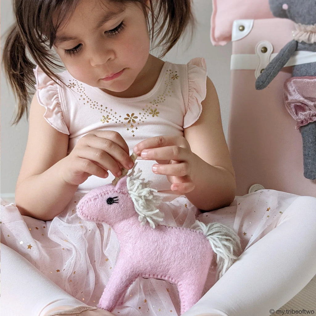 Young child holding the felt pink unicorn toy, showcasing its gentle texture and cuddly size for imaginative play.