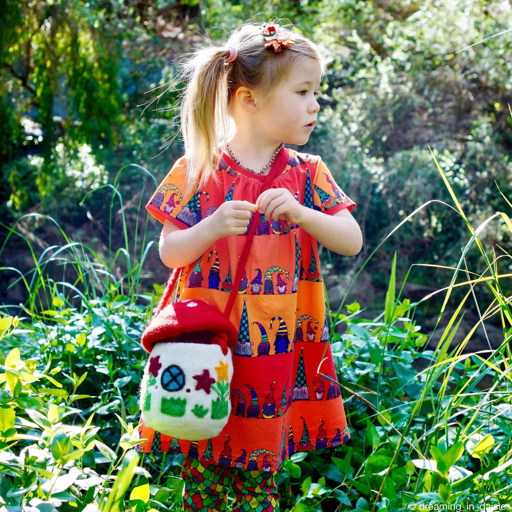 Young girl wearing the red mushroom bag in a garden, demonstrating adjustable strap and imaginative play use.