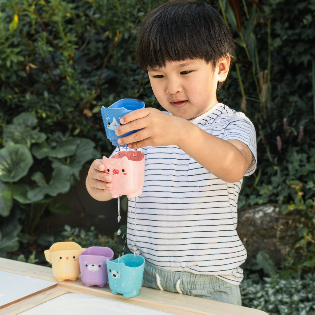 Child playing outdoors with the animal cups, stacking and pretending to pour, illustrating sensory exploration and imaginative play.