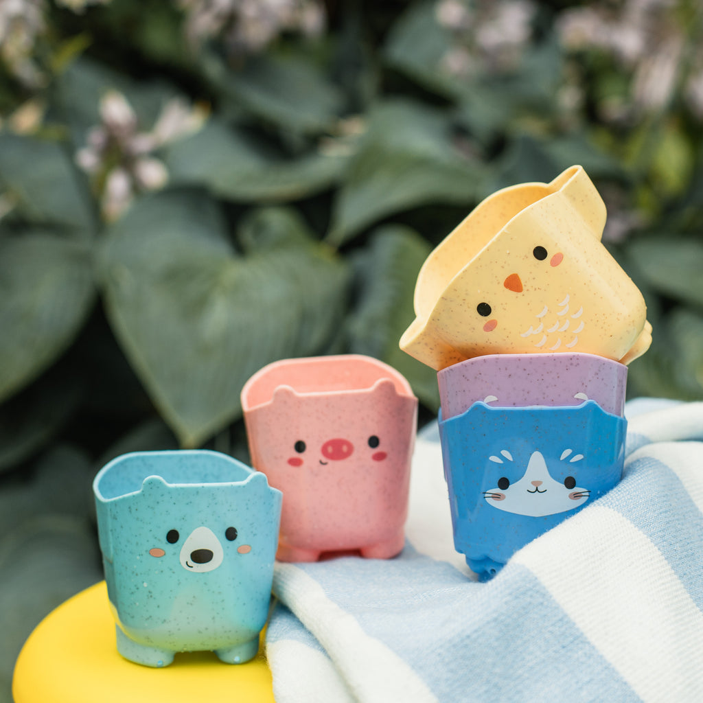 Animal cups lined up on a bathroom sink edge with their faces visible, ready for use during bath or water play.