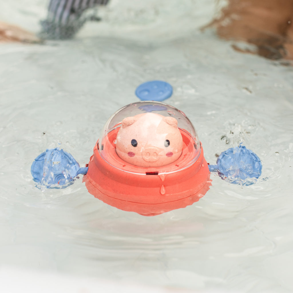 Space Piggy bath toy floating in water, paddling with side fins, demonstrating its movement and splashy fun during bath time.